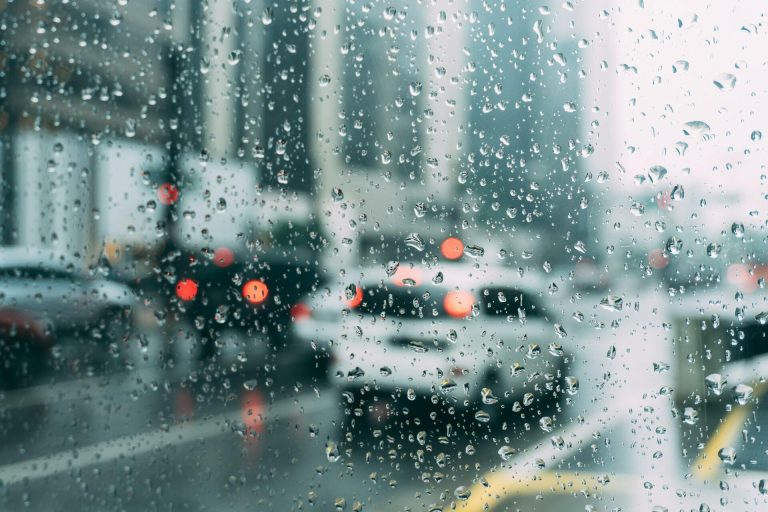 Rain-soaked city traffic blurred behind water droplets on a window.