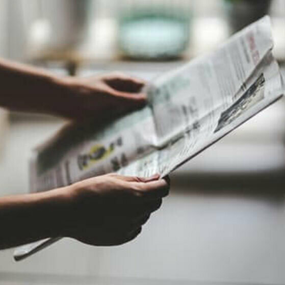 Hands holding and reading a folded newspaper.