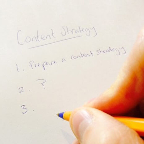 Hand holding a pencil beside a note titled “Content Strategy” with “1. Prepare a content strategy” written below.