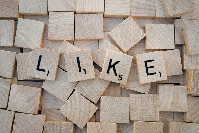 Wooden letter tiles spelling “LIKE” on a background of scattered tiles.