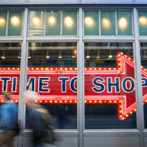 Neon arrow sign reading “TIME TO SHOP” behind a glass storefront.