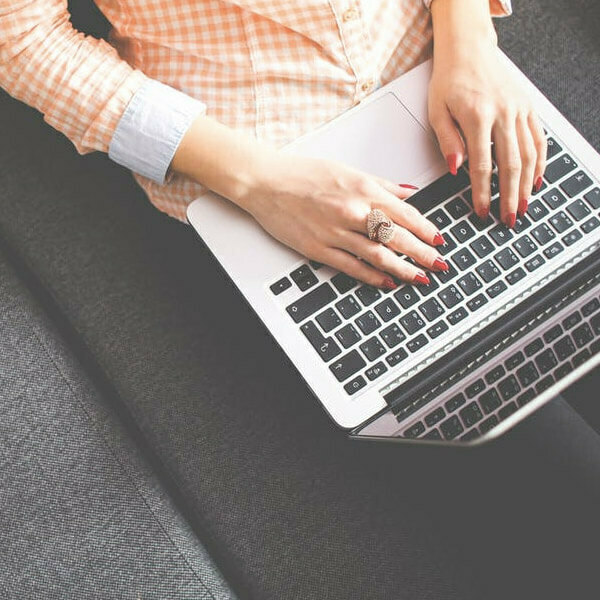 Woman typing on a laptop with red-painted nails while seated on a sofa.