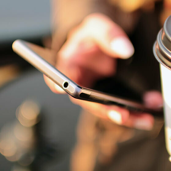 Hand using a smartphone beside a coffee cup.