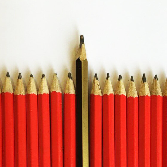 A single sharpened pencil stands out among a row of red pencils.