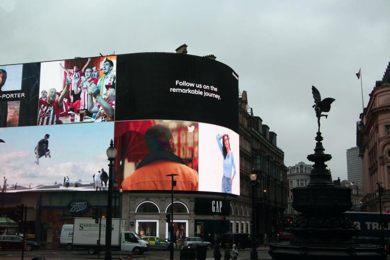 Piccadilly Circus with large digital billboards above a GAP store at dusk.