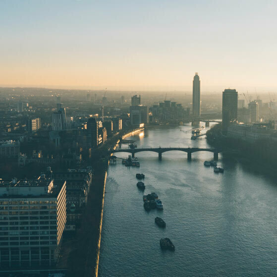 Sunrise over a city skyline and river with several bridges and boats.