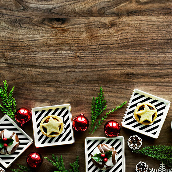 Festive flat lay of Christmas cookies, red baubles, and evergreen sprigs on a wooden table.