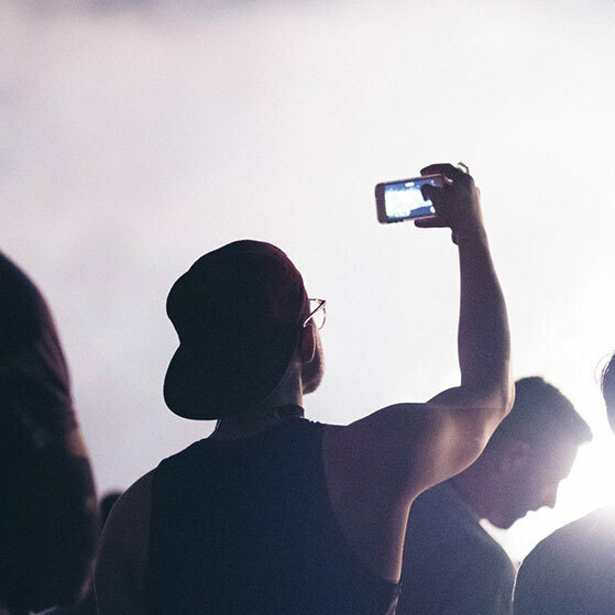 Person in a cap raises a smartphone to record a bright live event.