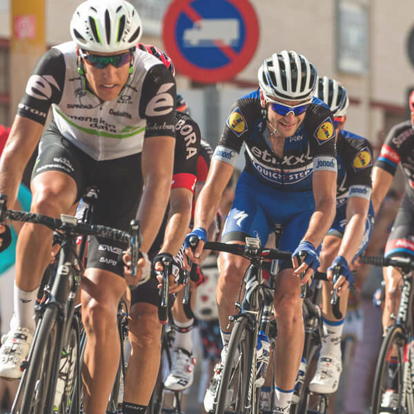 Cyclists in a road race riding tightly packed through a city street.