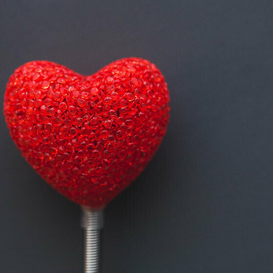 Red glitter heart ornament on a stick against a dark background.