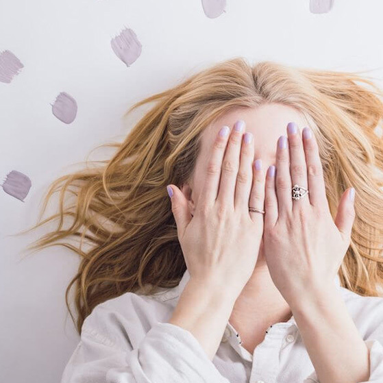 Woman lying on a white background with her face covered by her hands, surrounded by pale paint swatches.