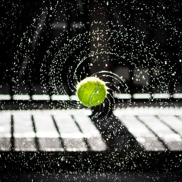 Tennis ball surrounded by water spray against a dark background.
