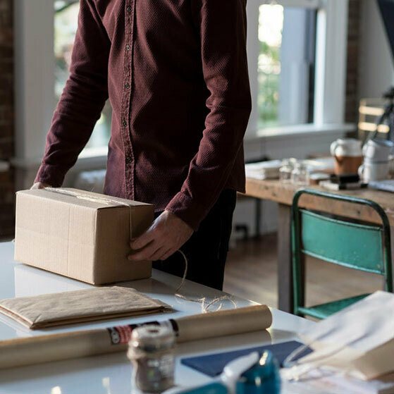 Person wrapping a cardboard box on a worktable in a studio.