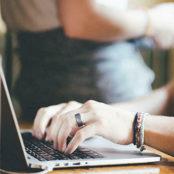 Hands typing on a laptop, wearing a ring and bracelets.