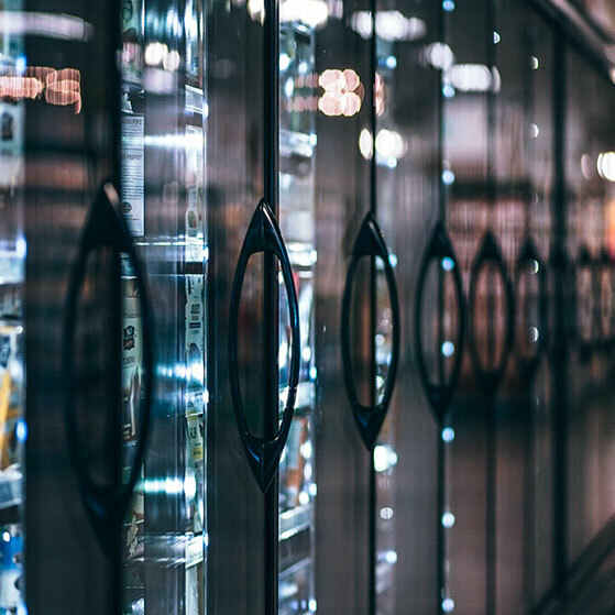 Row of glass refrigerator doors with black handles reflecting store lights.
