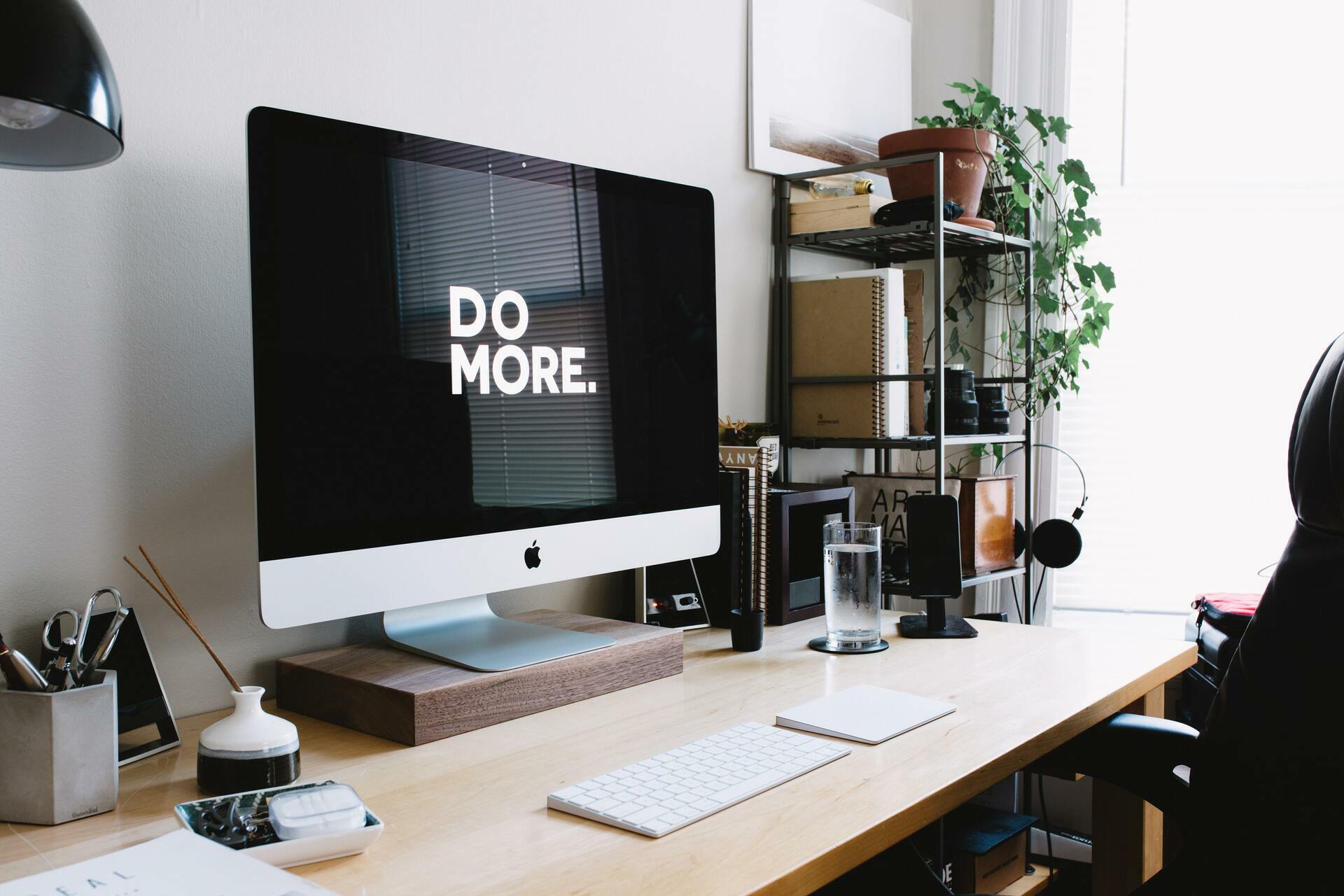 iMac on a tidy desk displaying “DO MORE” with plants and office accessories nearby