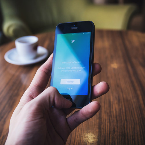 Hand holding a smartphone displaying Twitter’s welcome screen with Sign up and Log in buttons.