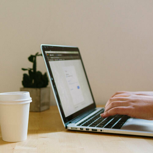 Hands typing on a laptop beside a takeaway coffee cup.