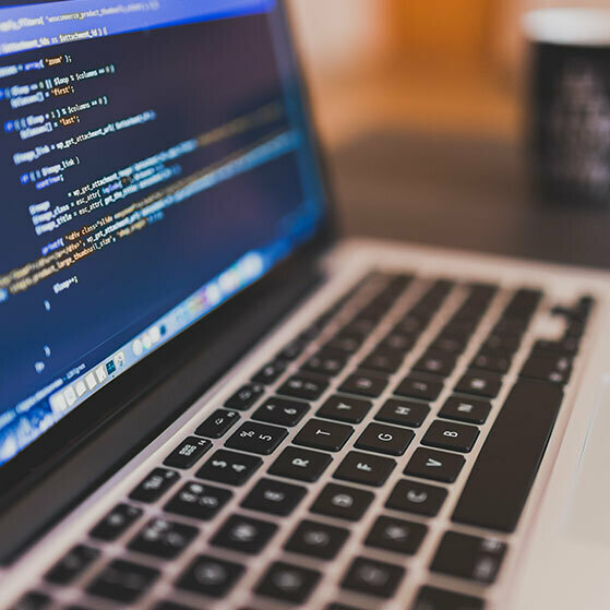 Laptop keyboard beside a screen displaying code in a text editor.