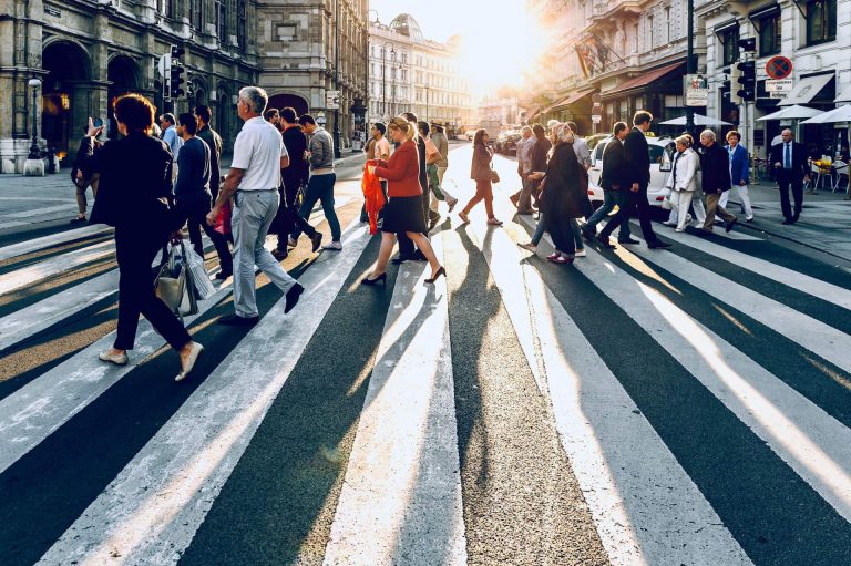 Pedestrians crossing a city street at a zebra crossing in bright evening sunlight.