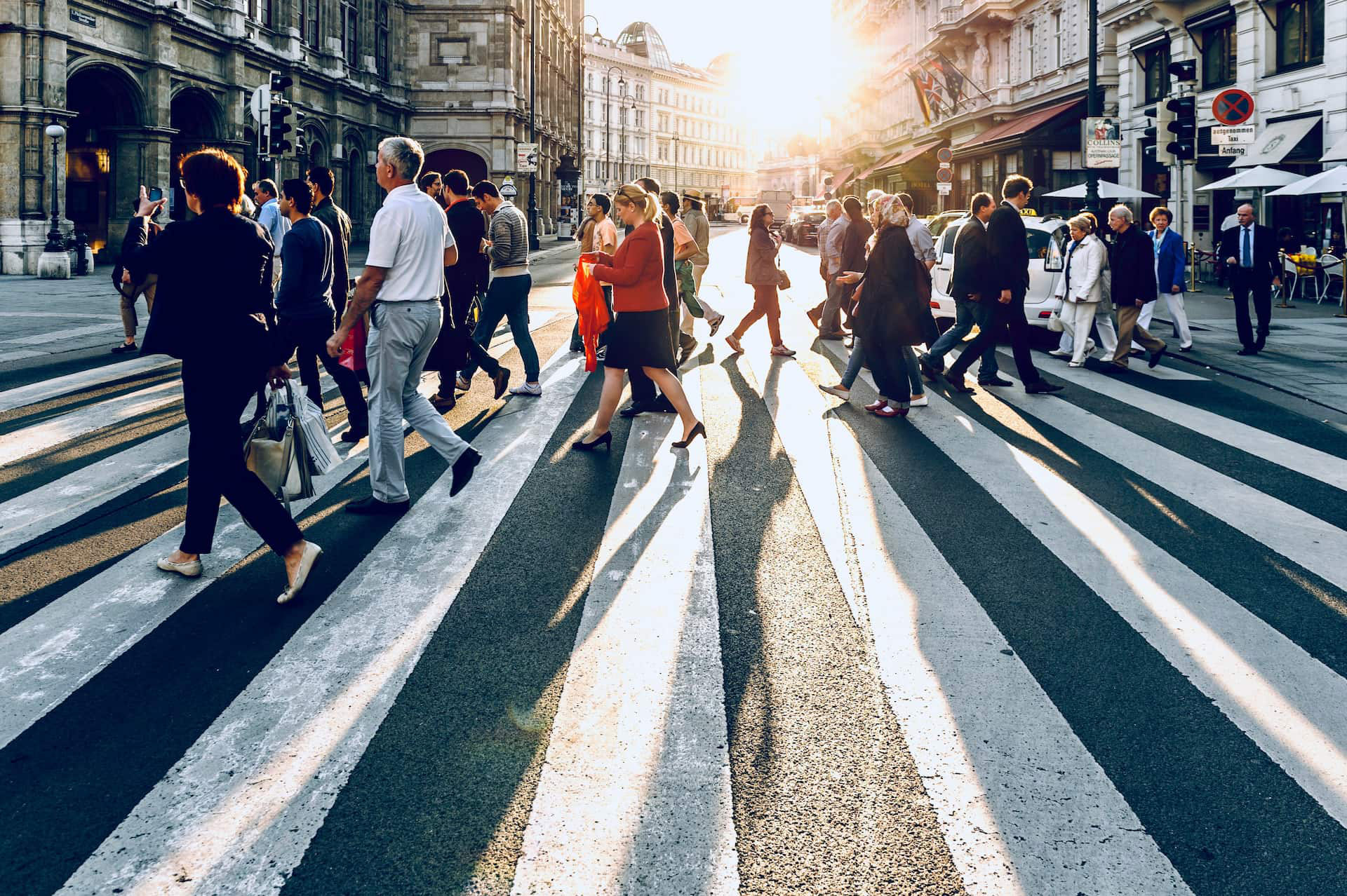 Pedestrians crossing a city street at a zebra crossing in bright evening sunlight.