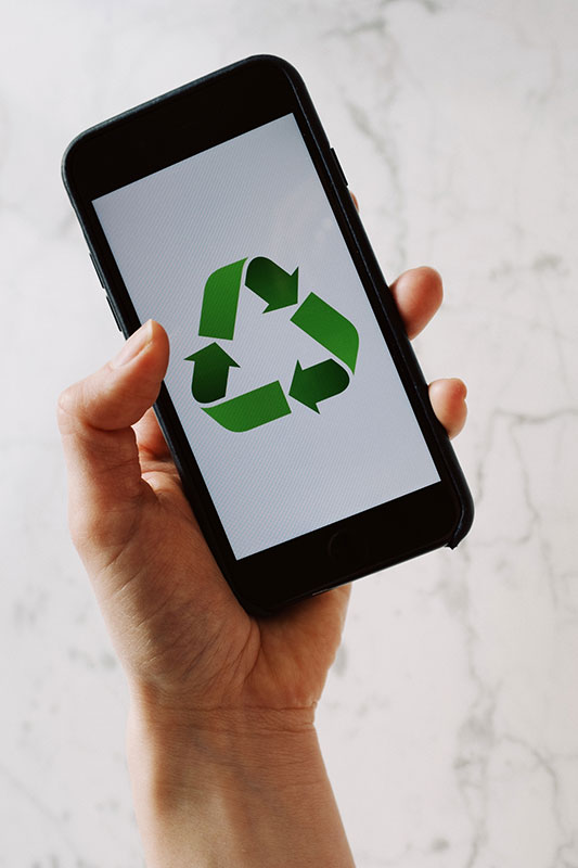 Hand holding a smartphone with a green recycling symbol on the screen.