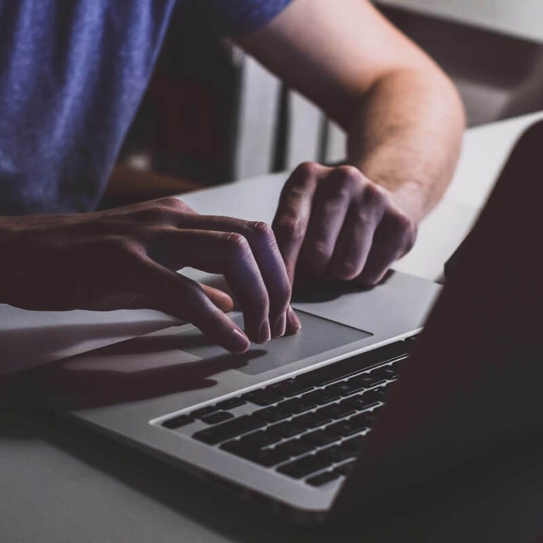Hands using a laptop trackpad in dim light.