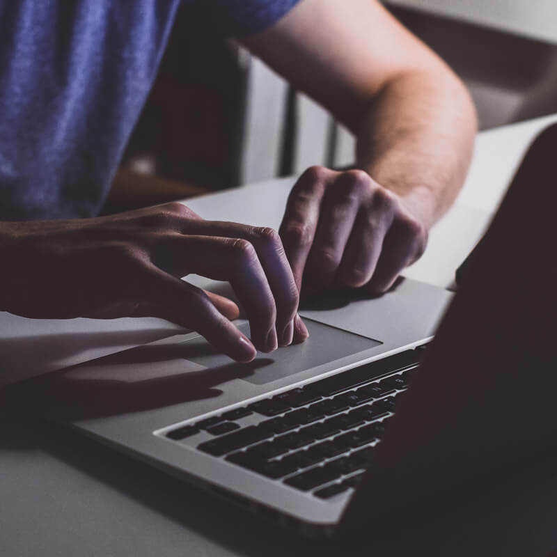 Hands using a laptop trackpad in dim light.