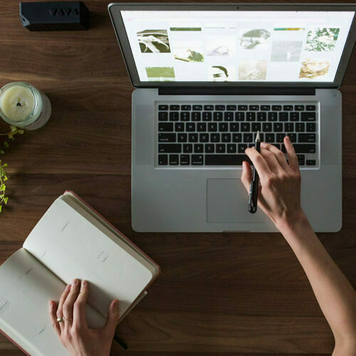 Hands working on a laptop beside an open notebook on a wooden desk.