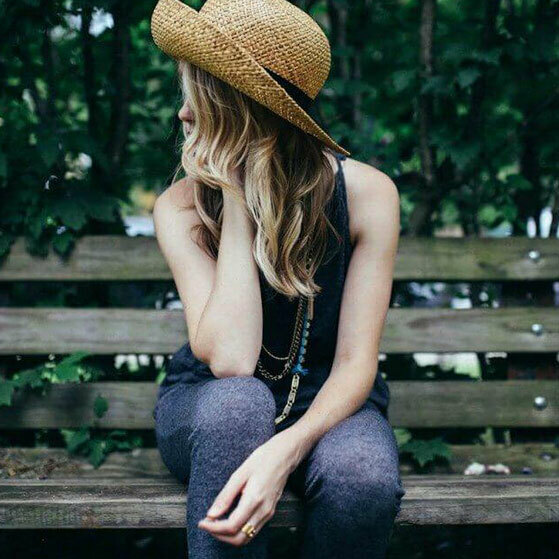 Woman in a straw hat sitting on a wooden bench and looking to the side.