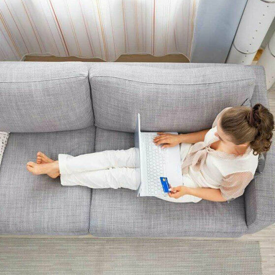 Child using a laptop on a sofa while holding a credit card.