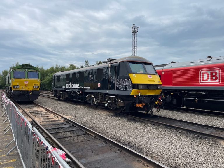 Black DB locomotive labeled “backbone of the economy” beside green and red trains on a rail siding.