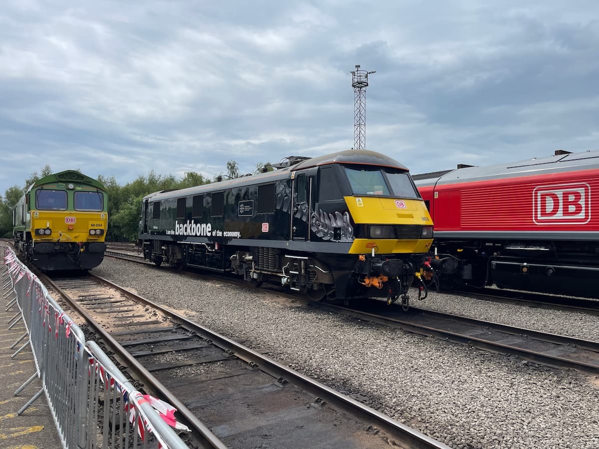 Black DB locomotive labeled “backbone of the economy” beside green and red trains on a rail siding.