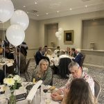 Guests seated at round tables in a formal dining room decorated with white balloons.
