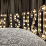 Illuminated marquee letters spelling “WISH2026” against curtains.