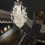 Grand staircase with a large crystal chandelier hanging over patterned carpet runners.