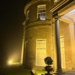 Grand stone building with a curved facade and lit columns at night.