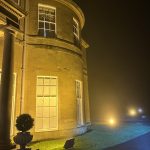 Illuminated historic stone building with rounded corner windows at night in mist.
