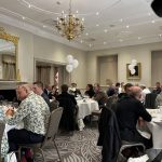 Guests seated at round tables in a chandelier-lit reception room with W20 balloons.
