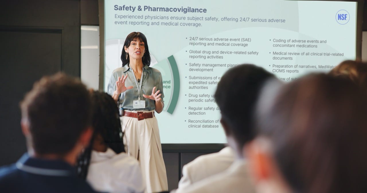 Presenter speaks at an NSF presentation slide titled “Safety & Pharmacovigilance” to an audience.